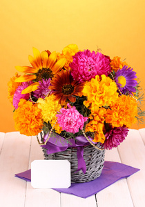 束美丽的鲜艳的花朵与在黄色背景上的木桌上的纸笔记