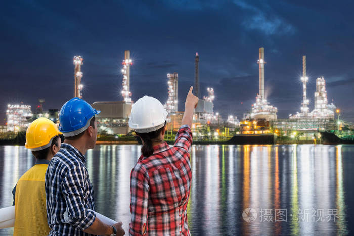 亚洲工程师小组在暮光之夜的天空中, 就石油或石化工业生产的石油和天然气炼油厂附近进行咨询。工程理念