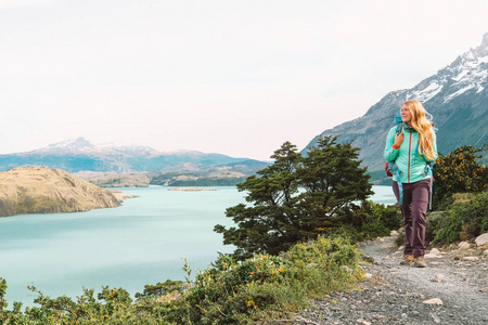 在绿色山脉和蓝色湖泊的背景下徒步旅行的金发女郎。智利。托雷斯