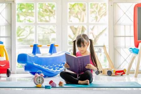 可爱的小女孩正在读一本书。有趣的孩子在孩子的房间里玩