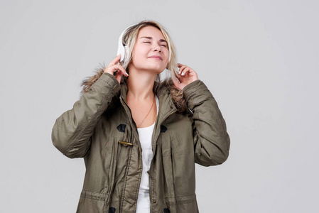 一个穿着秋季保暖夹克的年轻女孩在灰色背景上收听无线耳机上的音乐
