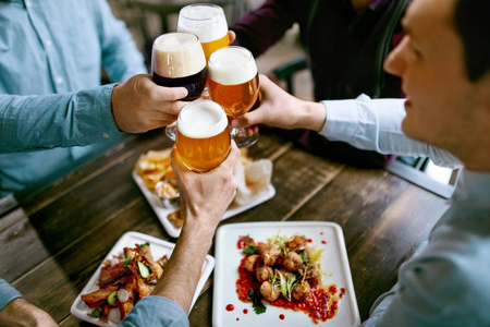 餐桌上的酒杯喝啤酒.朋友们在酒吧里用食物在餐桌上举起酒杯.