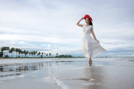 美丽的亚洲女孩穿着白色的礼服和红色的帽子在海滩上