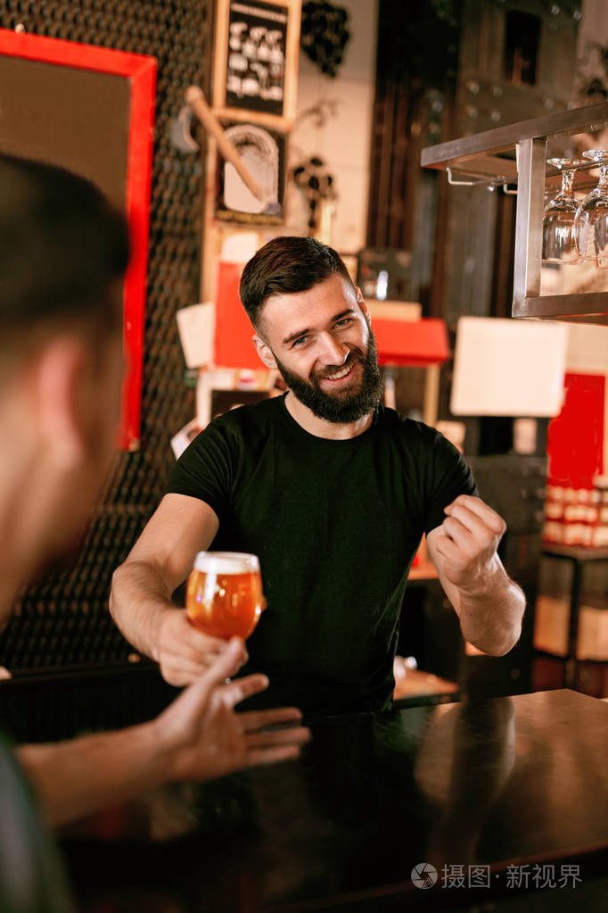酒吧里有啤酒的酒保.在酒吧工作的微笑的人高分辨率
