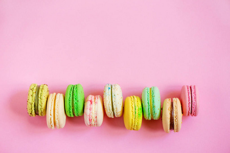 粉红色背景上的一排五颜六色的马卡龙.顶部视图.复制空间照片
