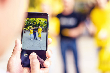 男人的手在手机上拍朋友的照片户外, 蓝色和黄色的颜色