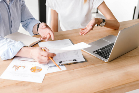 在办公室里用手提电脑和文书工作的集中的两个同事密切合作照片