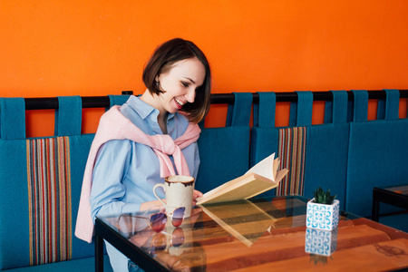 年轻漂亮的女人喝咖啡, 在咖啡馆里看书。色调