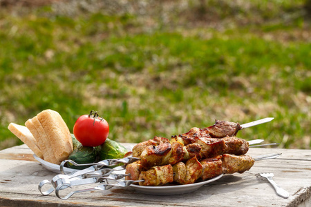 羊肉串烤肉串。在一张有新鲜蔬菜的木桌上。绿草背景下的烤肉串