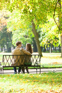 情侣在公园的长凳上坐在春天或秋天的一天