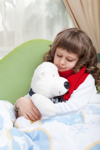 围巾的小病女孩拥抱在床上的玩具熊