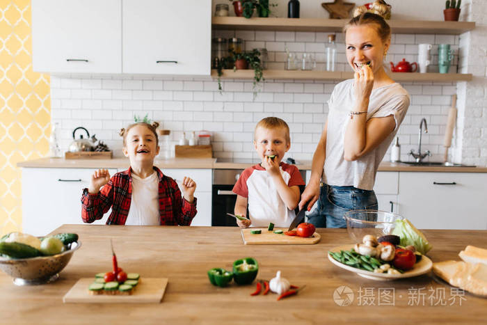 年轻母亲与女儿和儿子在餐桌上切菜的照片