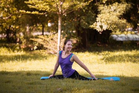 一位年轻女子微笑着在公园户外练习瑜伽。健康的生活方式和放松的概念