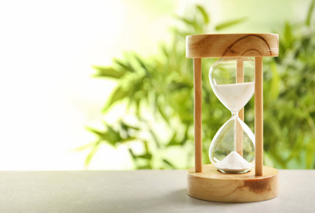 沙漏与流动的沙子在桌子上对模糊的背景.时间管理照片