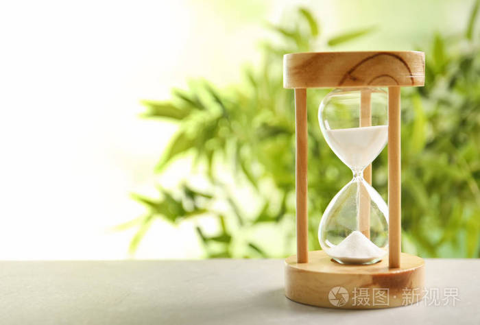 沙漏与流动的沙子在桌子上对模糊的背景时间管理