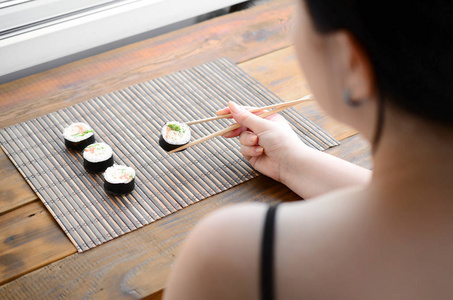 黑头发的女孩用筷子举行寿司卷在竹秸秆 serwing 垫背景。传统亚洲食品