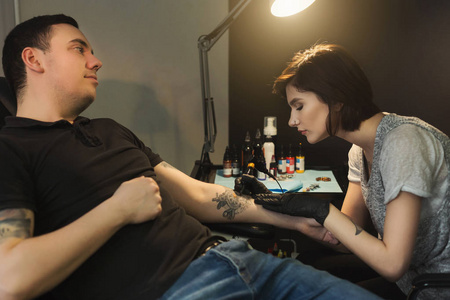 年轻女子 tattooist 在男性手臂上做纹身