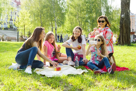 在公园休息。母亲带着孩子坐在草地上, 女人喝咖啡, 孩子们吃苹果