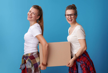微笑现代时髦的室友在白色衬衣拿着一个纸板盒一起孤立的蓝色背景