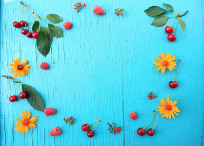 营养丰富的水果。新鲜的樱桃和覆盆子在蓝桌上特写和明亮的夏日花朵。从上面的水平视图。复制文本空间
