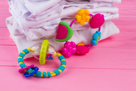 折叠婴儿衣服和玩具。婴儿摇铃, 粉红色的木质背景