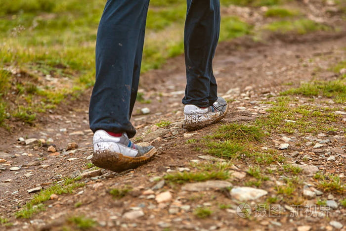 一只穿着白色运动鞋的年轻游客在山上的泥土路上行走的特写