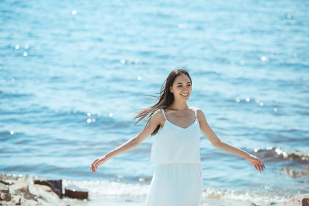 快乐亚洲妇女白色礼服以宽广的胳膊在海站立