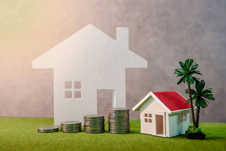不动产投资或住房抵押贷款利率。物业阶梯概念。硬币叠, 房子模型和表时钟在绿色草。投资和业务增长背景