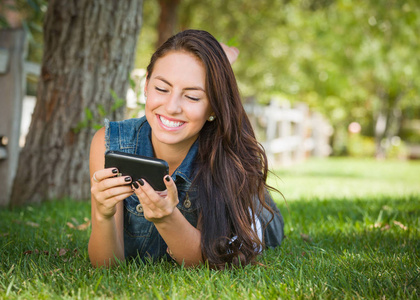 有吸引力的快乐混的血年轻女性发短信在她的手机外面躺在草地上