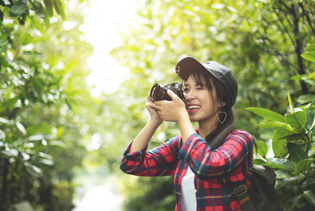 亚洲女孩旅行者在红色格子衬衣与复古照相机在森林里拍照。徒步。笑脸