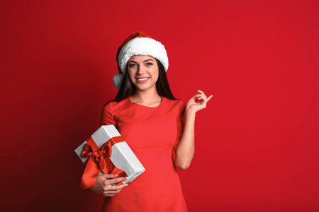 年轻漂亮的女子在圣诞老人的帽子与礼品盒的颜色背景。圣诞庆典