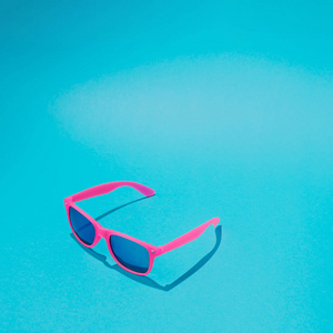 粉红色太阳镜在柔和的蓝色背景, 极小的夏天概念