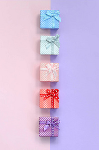 带丝带的不同颜色的小礼品盒位于紫罗兰色和粉红色背景上
