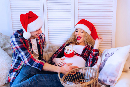 一个男人在圣诞老人的帽子和他的怀孕的妻子坐在沙发上