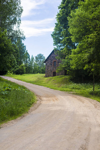 拉脱维亚一个晴朗晴朗的日子, 在乡间小路旁的一座古老的石屋, 穿过绿色的森林。