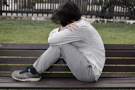 孤独沮丧的亚洲男人坐着, 抱着膝盖, 在长凳上哭泣.照片