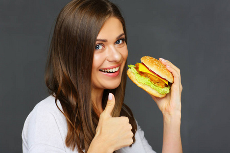 年轻有魅力的女人的肖像吃快餐汉堡和显示拇指