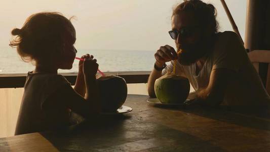 父亲和女儿坐在海景咖啡馆, 一起喝椰子