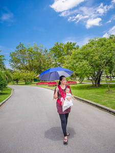 母亲和婴儿举起一把雨伞在公园里散步