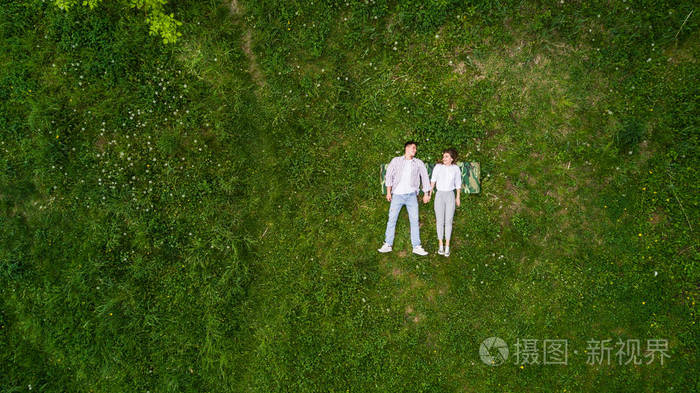 浪漫的情侣在公园草地上的年轻人躺在一起, 从上面看着手