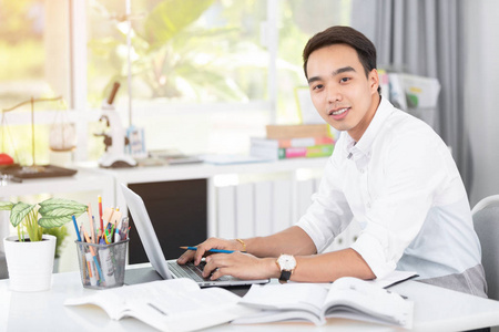 年轻的亚裔男子大学生与笔记本电脑和笔记本, 自学和大学生活的概念