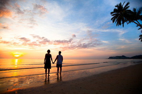 一对年轻夫妇在日落时在海边手牵手的爱照片