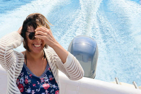 美丽的微笑快乐的年轻妇女与流头发在船上对蓝色的水和小船小径