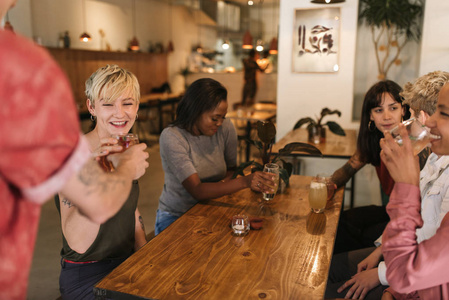 不同的一群微笑的年轻女性朋友坐在一个时髦的小酒馆的餐桌上接受侍者的饮料