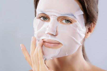 面部护理和美容护理。妇女用布保湿面具在她的脸上孤立的灰色背景