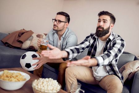 两位年轻的足球迷在家看电视上的足球