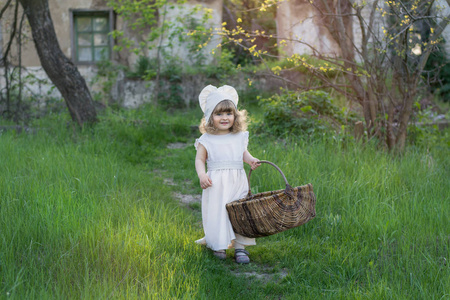 一个漂亮的小女孩在乡下散步。一个穿着白色连衣裙的孩子, 手里拿着柳条篮子。日落照片