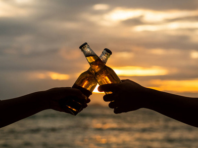 夫妇手拿着啤酒瓶, 在日落海滩上叮当响.