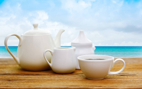 在美丽的热带海滩和海的木桌上的茶杯和壶茶与白云和蓝天背景假日假期概念