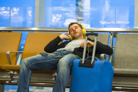 和疲惫的旅游男子与行李箱听音乐, 在登机门等待飞行假期旅行和假期